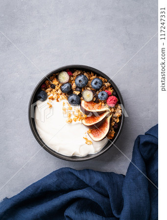 Delicious natural yogurt with granola and berries  in a bowl on a blue background.  117247331