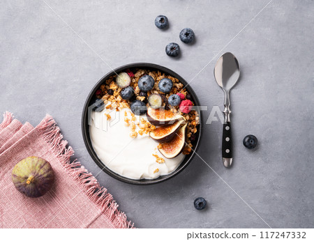 Natural yogurt with granola, berries and figs in a bowl on a blue background. Natural yogurt with granola, berries and figs in a bowl on a blue background. 117247332