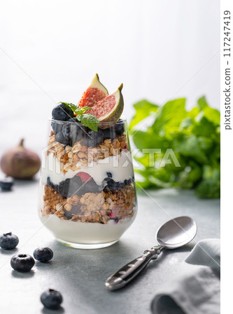 Delicious natural yogurt with granola and berries  in a glass on a blue background. 117247419