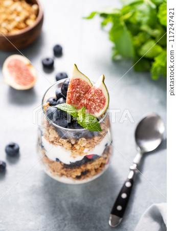 Delicious natural yogurt with granola, figs and berries in a glass on a blue background. Delicious natural yogurt with granola, figs and berries in a glass on a blue background. 117247421