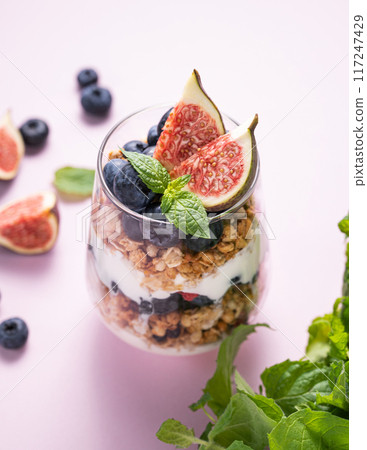 Delicious natural yogurt with granola, figs and blueberries in a glass on a pink background Delicious natural yogurt with granola, figs and blueberries in a glass on a pink background 117247429