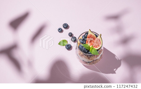 Delicious natural yogurt with granola, figs and blueberries in a glass on a pink background Delicious natural yogurt with granola, figs and blueberries in a glass on a pink background 117247432