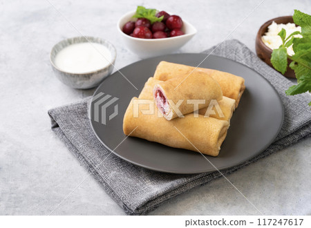 Homemade crepes with chery berry and a cottage cheese on a plate on a blue background Homemade crepes with chery berry and a cottage cheese on a plate on a blue background 117247617