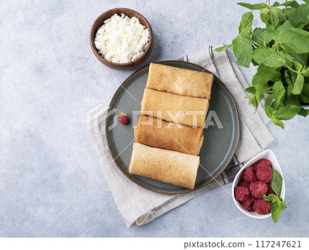 Homemade crepes with raspberry and a cottage cheese on a plate on a blue background. 117247621