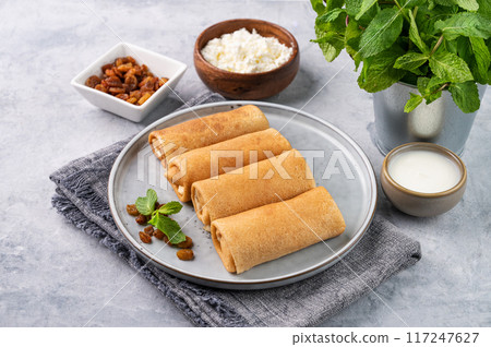 Homemade crepes with cottage cheese and raisin on a plate on a blue background with sour cream Homemade crepes with cottage cheese and raisin on a plate on a blue background with sour cream 117247627