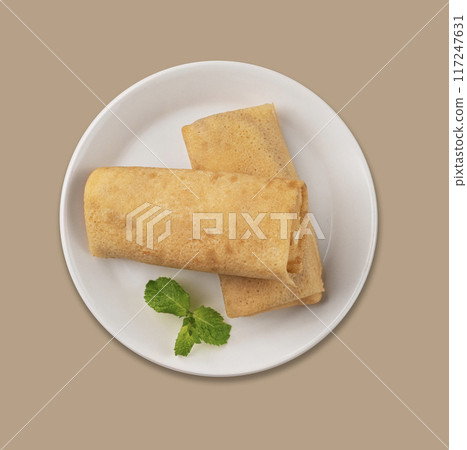 Homemade roll crepes with cottage cheese and mint on a white plate on a beige  background.  117247631