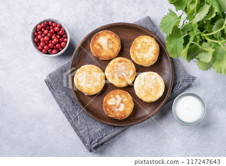 Pancakes with cottage cheese with fresh blerries and sour cream on a wooden plate  117247643