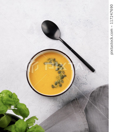 Autumn vegetarian pumpkin soup with cream and seeds on white background with fresh herbal and spoon Autumn vegetarian pumpkin soup with cream and seeds on white background with fresh herbal and spoon 117247690