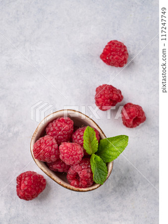 Juicy forest raspberry with mint leaf i a bowl on a light textured background. Healthy food concept Juicy forest raspberry with mint leaf i a bowl on a light textured background. Healthy food concept 117247749