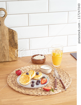 Cheesecakes or cottage cheese with fresh berries, sour cream and orange juice on a kitchen table. 117247840