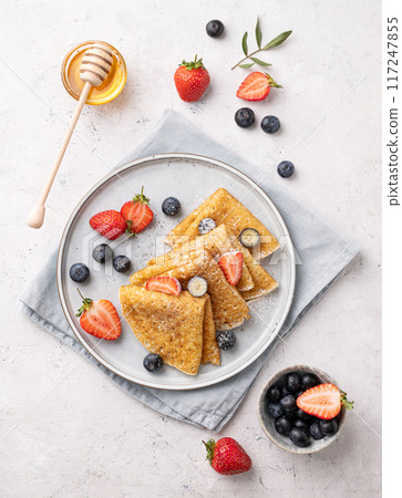 Flat lay homemade thin pancakes or crepes with fresh blueberries and strawberries and honey Flat lay homemade thin pancakes or crepes with fresh blueberries and strawberries and honey 117247855