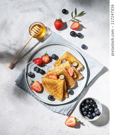 Homemade thin pancakes or crepes with fresh blueberries and strawberries and honey on a plate 117247856