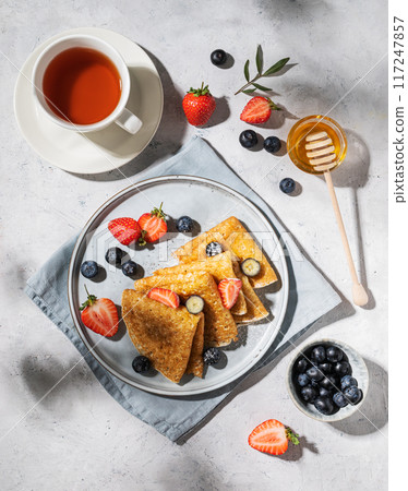 Homemade thin pancakes or crepes with fresh blueberries and strawberries, honey and cup of tea 117247857