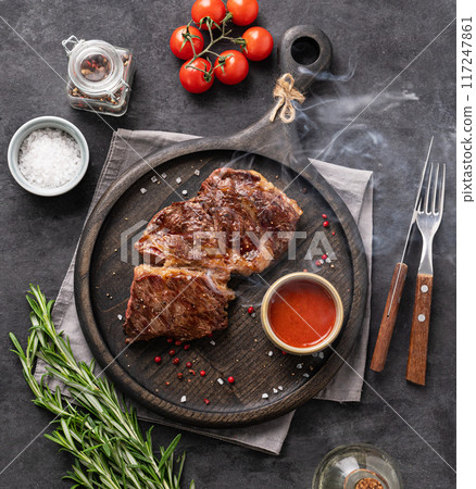 BBQ  beef steak grill with smoke, sauce, tomatoes, salt and rosemary on black wooden board  117247861