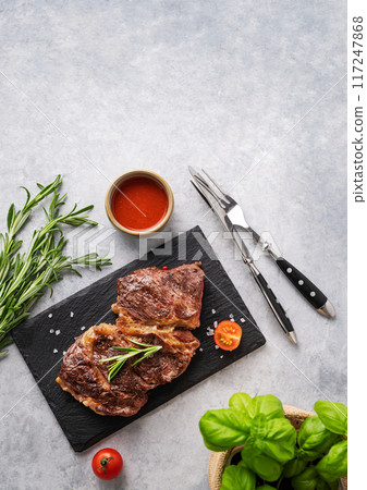 BBQ grilled beef steak with sauce, rosemary and basil on black slate on light  background. 117247868