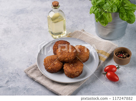 Chicken cutlets, fried, on a plate on a light background with fresh herbs, oil and tomatoes.  117247882