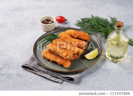 Fish fillet sticks  fried on a green plate with lime and fresh herb on a light background 117247889