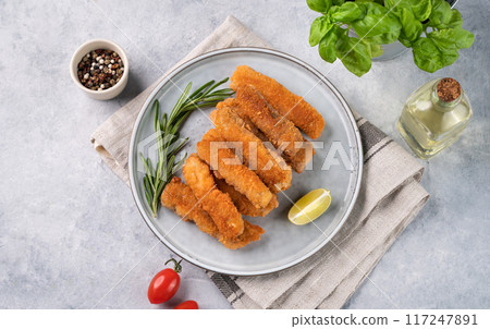 Fish fillet sticks fried on a plate with rosemary on a light background with tomatoes and spices. Fish fillet sticks fried on a plate with rosemary on a light background with tomatoes and spices. 117247891
