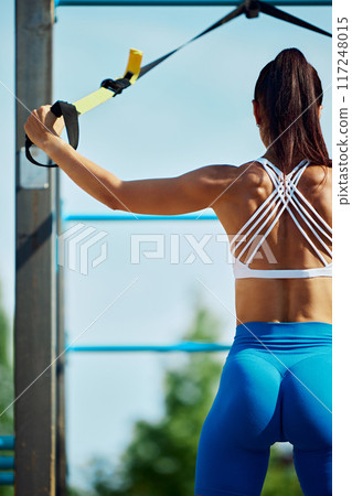 Beautiful young woman in sportswear doing trx exercises at park, outdoor gym. Person doing suspension training. Beautiful young woman in sportswear doing trx exercises at park, outdoor gym. Person doing suspension training. 117248015