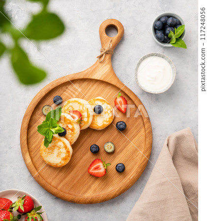 Cheesecakes or cottage cheese with fresh blerries and sour cream on a wooben board Cheesecakes or cottage cheese with fresh blerries and sour cream on a wooben board 117248056