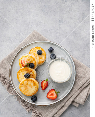 cheesecakes or cottage cheese or syrniki with fresh blerries and sour cream on a gray background. cheesecakes or cottage cheese or syrniki with fresh blerries and sour cream on a gray background. 117248057