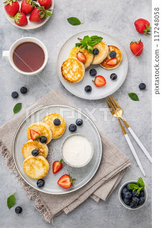 Pancakes with cottage cheese or syrniki with fresh blerries and sour cream on a gray background Pancakes with cottage cheese or syrniki with fresh blerries and sour cream on a gray background 117248058