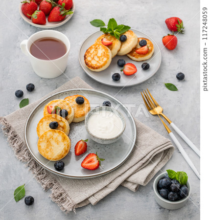 Pancakes with cottage cheese or syrniki with fresh blerries and sour cream on a gray background Pancakes with cottage cheese or syrniki with fresh blerries and sour cream on a gray background 117248059
