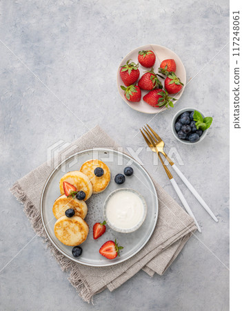 Cheesecakes or cottage cheese with fresh blerries and sour cream on a gray background. Cheesecakes or cottage cheese with fresh blerries and sour cream on a gray background. 117248061
