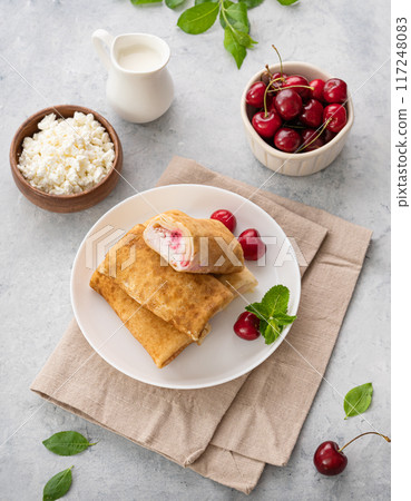 Delicious homemade pancakes or crepes with cottage cheese and fresh cherries on a white plate Delicious homemade pancakes or crepes with cottage cheese and fresh cherries on a white plate 117248083