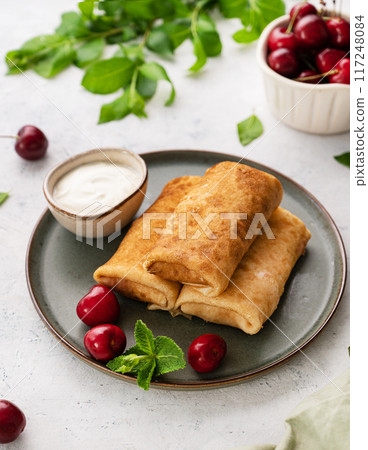 Delicious homemade pancakes or crepes with fresh cherries and sour cream on a dark plate Delicious homemade pancakes or crepes with fresh cherries and sour cream on a dark plate 117248084