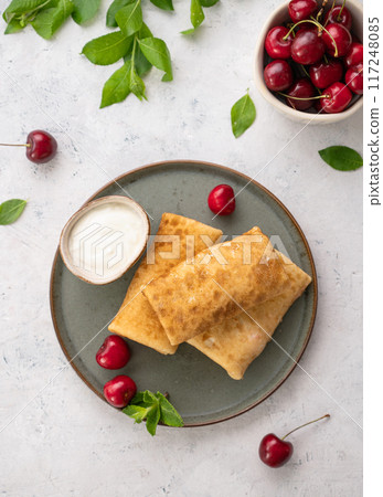 Delicious homemade pancakes or crepes  with fresh cherries and sour cream on a dark plate  117248085