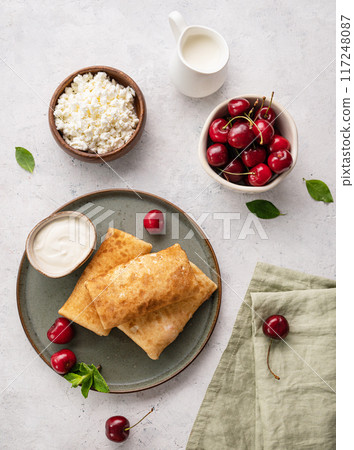Delicious homemade pancakes or crepes  with cottage cheese and fresh cherries on a green  plate 117248087