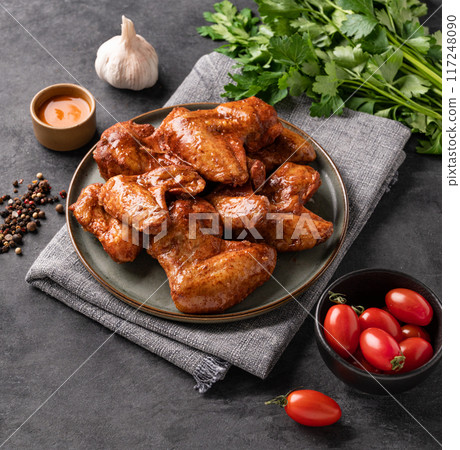 Spicy grilled chicken wings with sauce on a plate with tomato and herb on a dark background  117248090