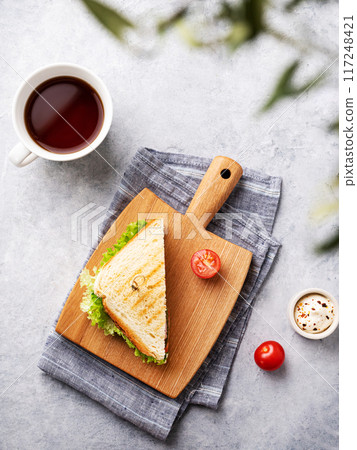 Club sandwich on a wooden board of ham, cheese, tomato and lettuce leaves on a blue background Club sandwich on a wooden board of ham, cheese, tomato and lettuce leaves on a blue background 117248421