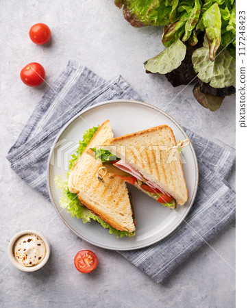 Club sandwich on a blue plate and napkin of ham cheese, cucumber, tomato and lettuce leaves close-up Club sandwich on a blue plate and napkin of ham cheese, cucumber, tomato and lettuce leaves close-up 117248423