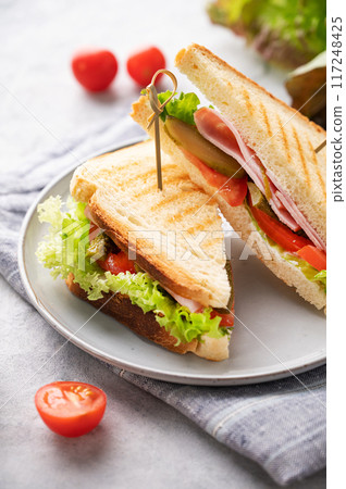 Club sandwich on a plate of ham cheese, cucumber, tomato and lettuce leaves close-up  117248425