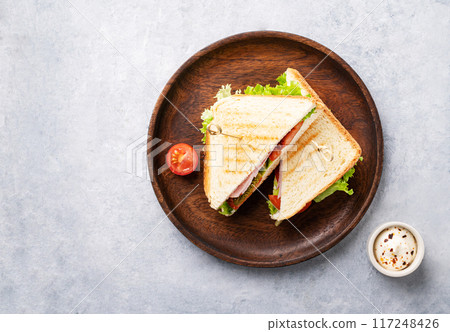 Club sandwich on a wooden plate of ham cheese, cucumber, tomato and lettuce leaves  117248426