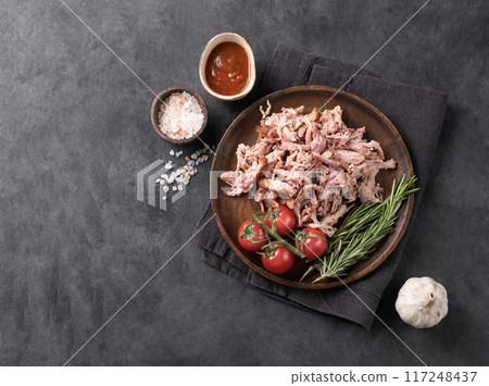 Traditional barbecue torn pork meat with bbq sauce, fresh tomatoes and herbs on a dark background. Traditional barbecue torn pork meat with bbq sauce, fresh tomatoes and herbs on a dark background. 117248437