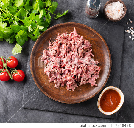 Traditional barbecue torn beef or lamb meat on wooden plate with bbq sauce, fresh tomatoes and herbs Traditional barbecue torn beef or lamb meat on wooden plate with bbq sauce, fresh tomatoes and herbs 117248438