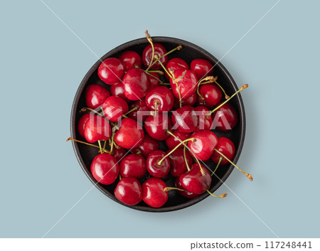 Juicy cherries in a black bowl on a blue background. Top view and copy space 117248441