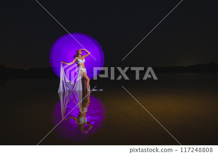 Young slim girl posing in water with abstract purple light effect Young slim girl posing in water with abstract purple light effect 117248808