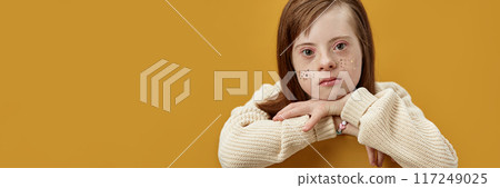 Minimal header image of cute young girl with disability with glitter freckles looking at camera over yellow background, copy space 117249025