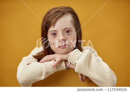 Portrait of girl with light brown hair and freckles leaning on her hands against yellow background portraying a calm and thoughtful expression 117249026
