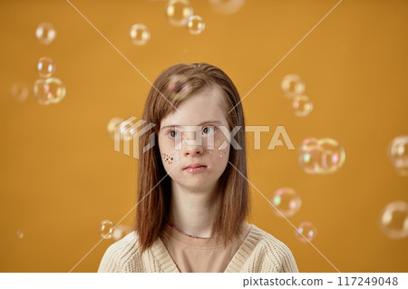 Young girl with Down syndrome surrounded by floating bubbles, creating a whimsical and joyful atmosphere against a golden background, wearing a subtle smile Young girl with Down syndrome surrounded by floating bubbles, creating a whimsical and joyful atmosphere against a golden background, wearing a subtle smile 117249048