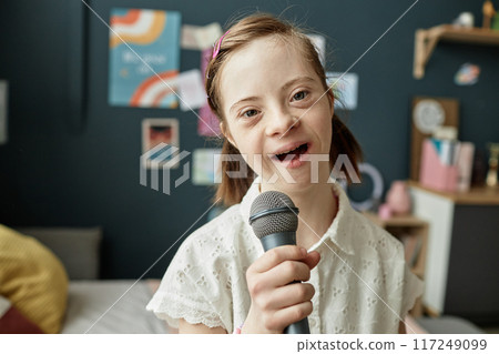 Portrait of smiling girl holding a microphone in cozy room with colorful decorations and bookshelf in background singing activity Portrait of smiling girl holding a microphone in cozy room with colorful decorations and bookshelf in background singing activity 117249099