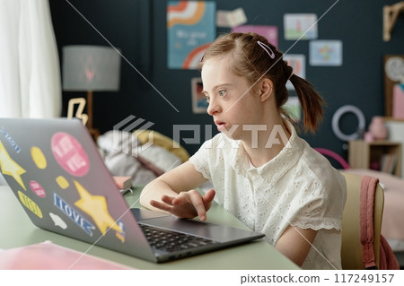 Girl using laptop in cozy room decorated with artwork and a lamp, focusing on screen and working diligently while sitting at desk with curtain letting in light without casting shadows 117249157