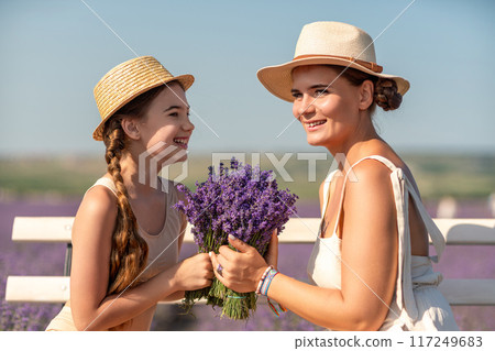 A woman and a child are sitting on a bench in a field of purple flowers lavande. The woman is holding a bouquet of flowers and the child is holding a bouquet of flowers as well A woman and a child are sitting on a bench in a field of purple flowers lavande. The woman is holding a bouquet of flowers and the child is holding a bouquet of flowers as well 117249683