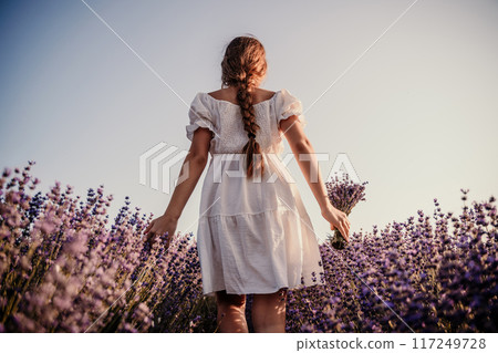 Lavender field girl. Back view happy girl in white dress with a scythe runs through a lilac field of lavender. Aromatherapy travel 117249728