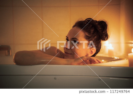 A woman is sitting in a bathtub with candles lit around her. She is smiling and she is enjoying her time. 117249764