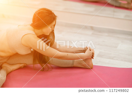 Girl does yoga. Young woman practices asanas on a beige one-ton background. Girl does yoga. Young woman practices asanas on a beige one-ton background. 117249802